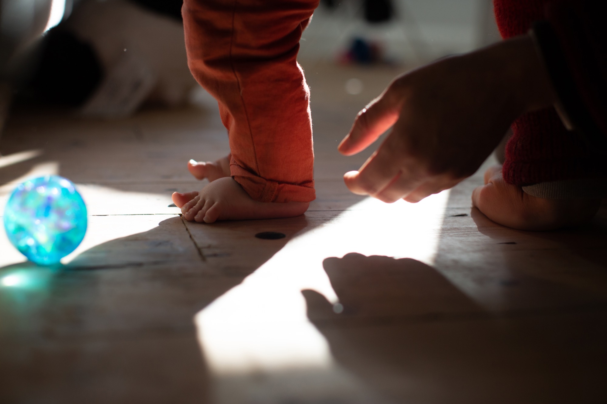 Sunlight falls across the floorboards where a baby plays with a glass ball.