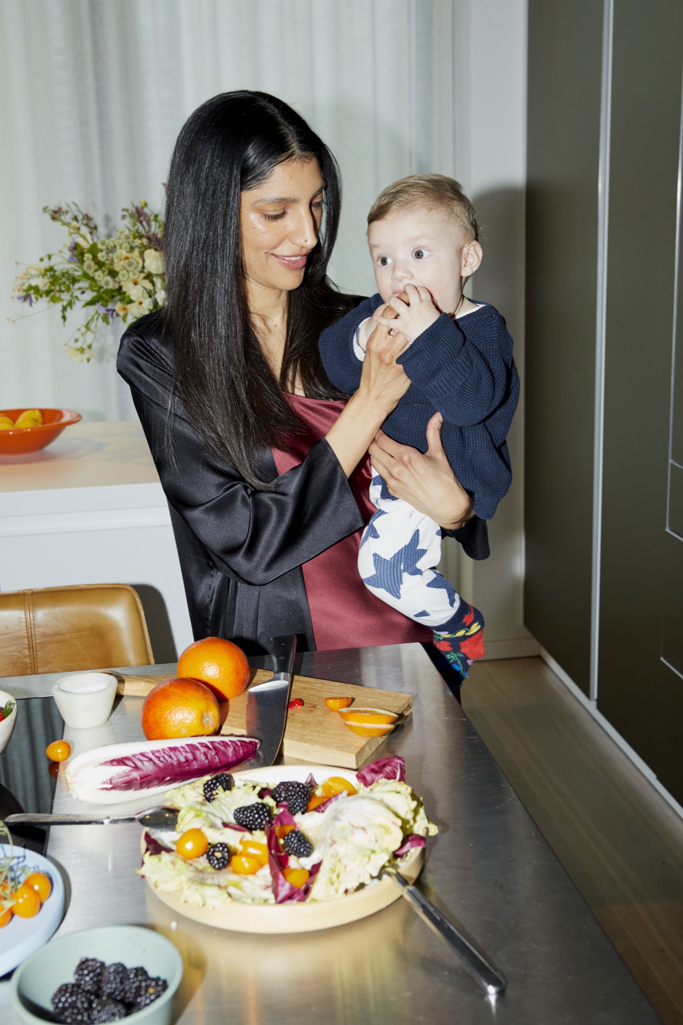 A mother sets the dinner table with her baby on her arm.